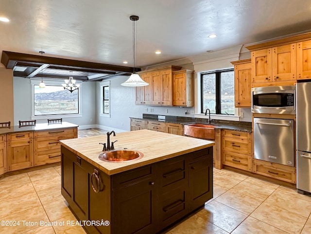 kitchen with a center island with sink, pendant lighting, stainless steel appliances, and wooden counters