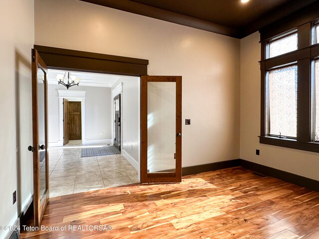 unfurnished room featuring french doors, light wood-type flooring, ornamental molding, and a notable chandelier