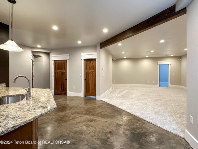 kitchen featuring decorative light fixtures, beam ceiling, light stone counters, and sink