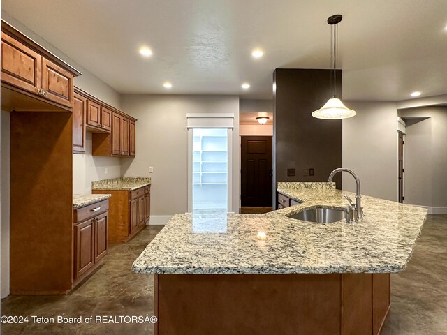 kitchen with pendant lighting, light stone countertops, sink, and a kitchen island with sink