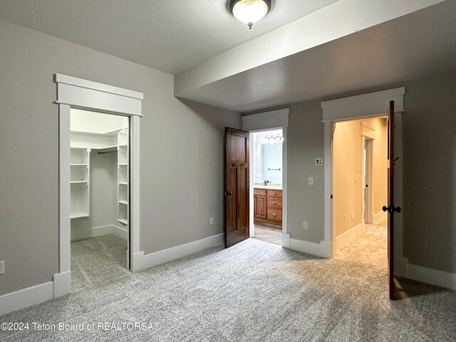 unfurnished bedroom with a closet, light colored carpet, a spacious closet, and ensuite bath