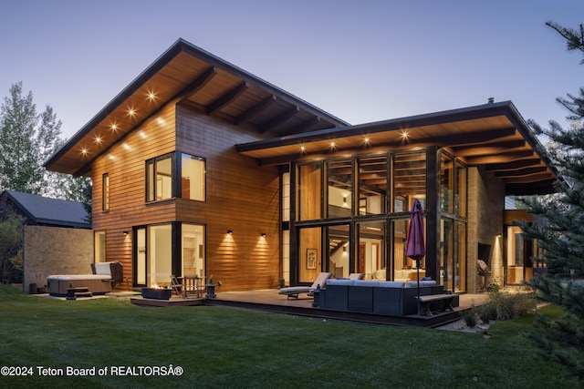 back house at dusk featuring a lawn, outdoor lounge area, a sunroom, and a hot tub