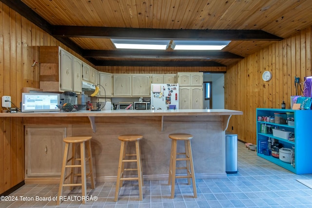 kitchen featuring white refrigerator, wood ceiling, a breakfast bar area, and wood walls