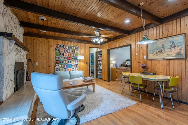 living room featuring beamed ceiling, wooden walls, and light hardwood / wood-style flooring