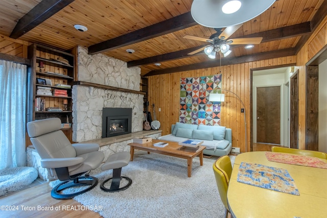 carpeted living room featuring beamed ceiling, a fireplace, ceiling fan, and wooden walls