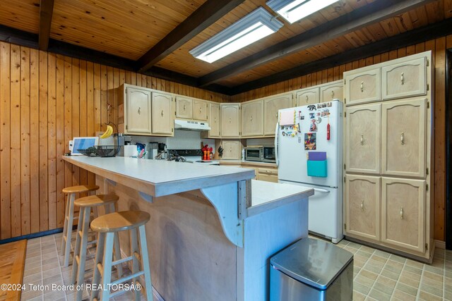 kitchen featuring kitchen peninsula, black range oven, a breakfast bar, beam ceiling, and white fridge