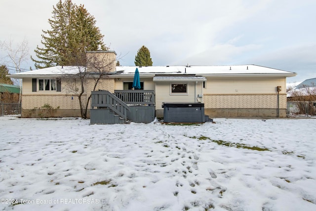 snow covered back of property with a hot tub and a deck