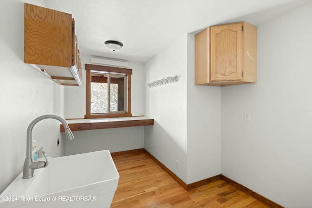 laundry room featuring cabinets, sink, and light hardwood / wood-style flooring