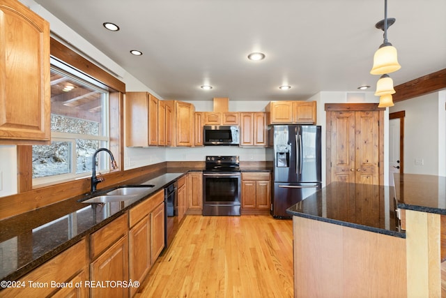 kitchen with hanging light fixtures, sink, dark stone countertops, appliances with stainless steel finishes, and light hardwood / wood-style floors