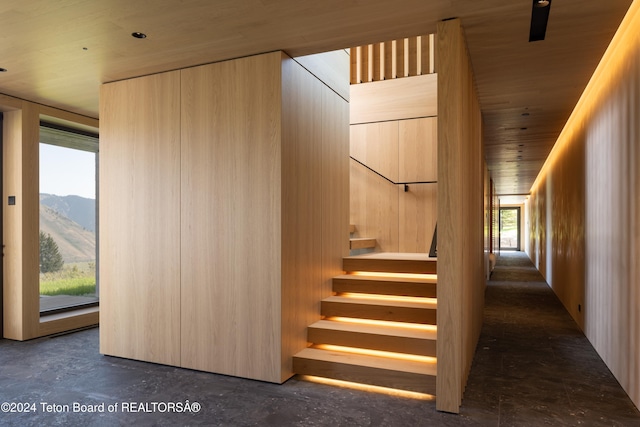 stairway featuring concrete flooring, wood ceiling, a mountain view, and wood walls