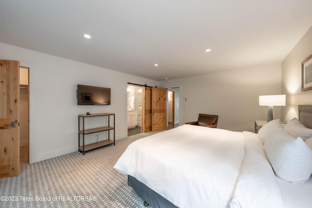 bedroom with a spacious closet, a barn door, ensuite bathroom, light carpet, and a closet