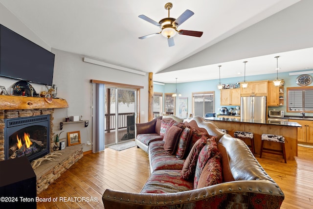 living room with high vaulted ceiling, ceiling fan with notable chandelier, a stone fireplace, sink, and light wood-type flooring