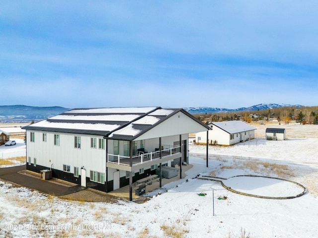 snow covered house featuring a mountain view and a balcony