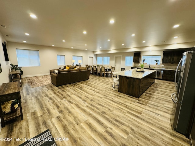 kitchen featuring light stone countertops, appliances with stainless steel finishes, light wood-type flooring, a breakfast bar, and a kitchen island