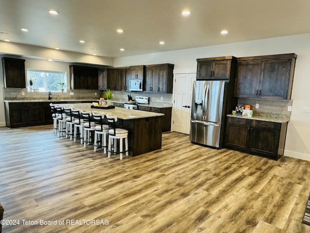 kitchen with light wood-type flooring, backsplash, a breakfast bar, stainless steel appliances, and a center island