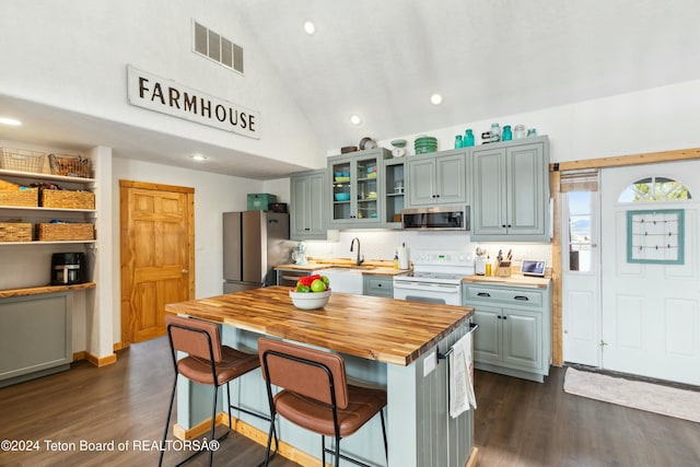 kitchen with appliances with stainless steel finishes, sink, butcher block countertops, dark hardwood / wood-style floors, and a breakfast bar area