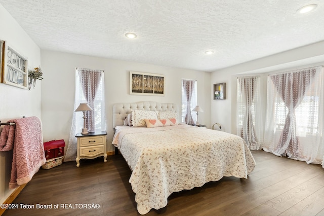 bedroom with a textured ceiling, dark hardwood / wood-style floors, and multiple windows