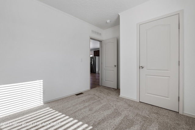 unfurnished bedroom with stainless steel refrigerator with ice dispenser, a textured ceiling, light colored carpet, and crown molding