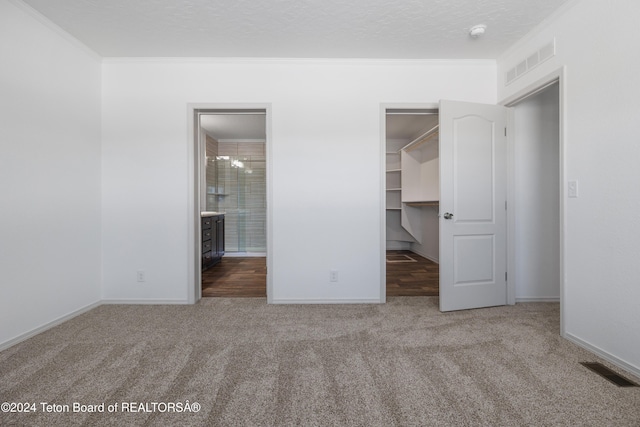 unfurnished bedroom featuring a walk in closet, carpet flooring, ornamental molding, a textured ceiling, and connected bathroom