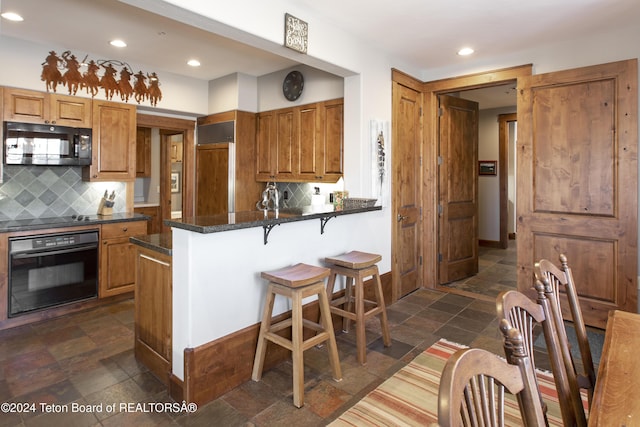 kitchen featuring tasteful backsplash, kitchen peninsula, a breakfast bar area, and black appliances