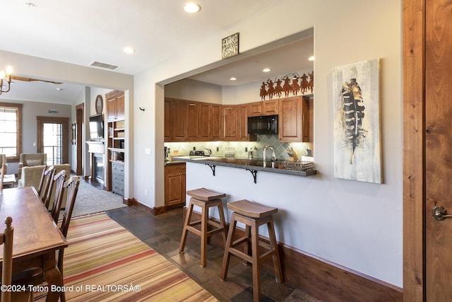 kitchen with sink, backsplash, kitchen peninsula, a breakfast bar area, and dark carpet