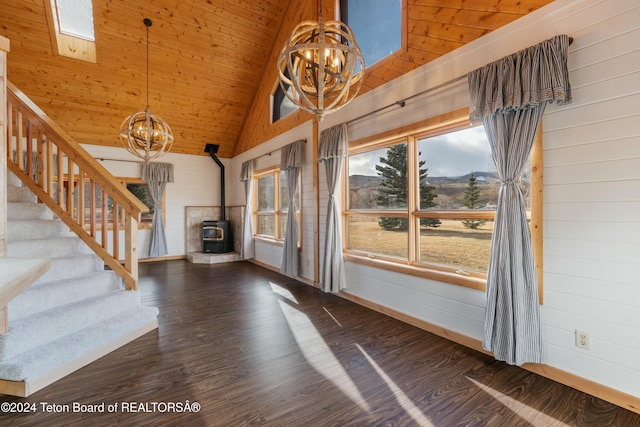 unfurnished living room featuring dark hardwood / wood-style flooring, a wood stove, a notable chandelier, and wood walls