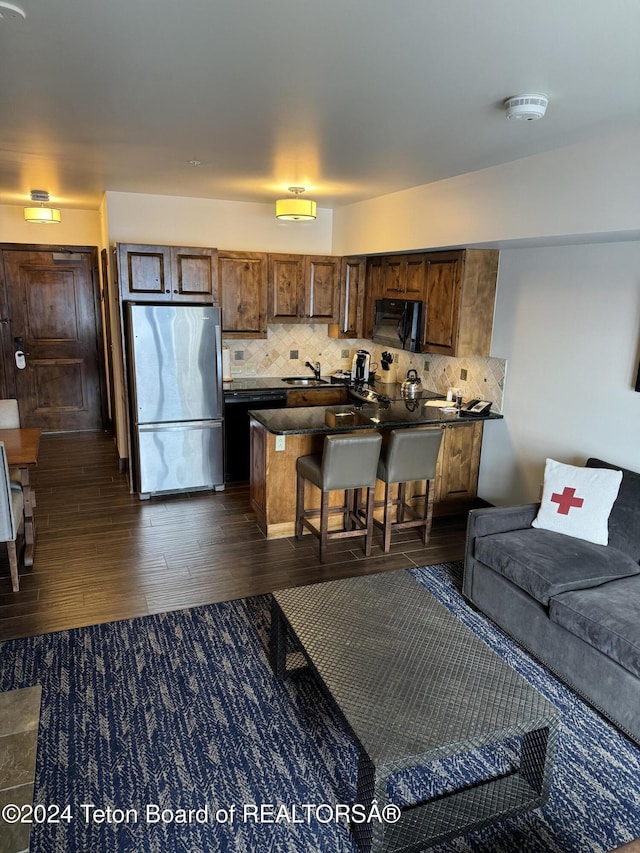 kitchen with a peninsula, freestanding refrigerator, a sink, black microwave, and dark countertops