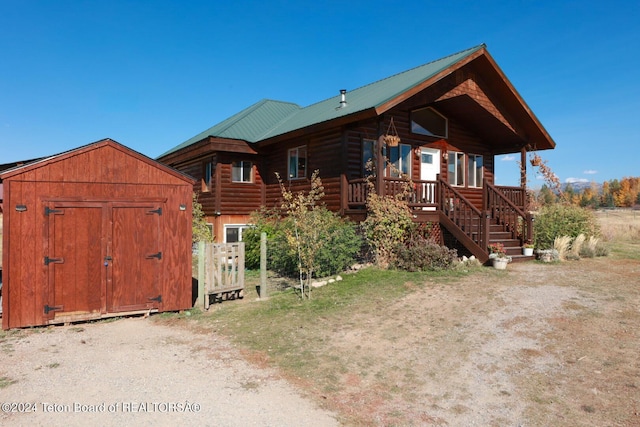 log-style house featuring covered porch and a storage shed