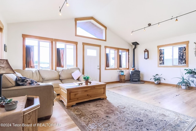 living room featuring plenty of natural light, light hardwood / wood-style floors, a wood stove, and high vaulted ceiling