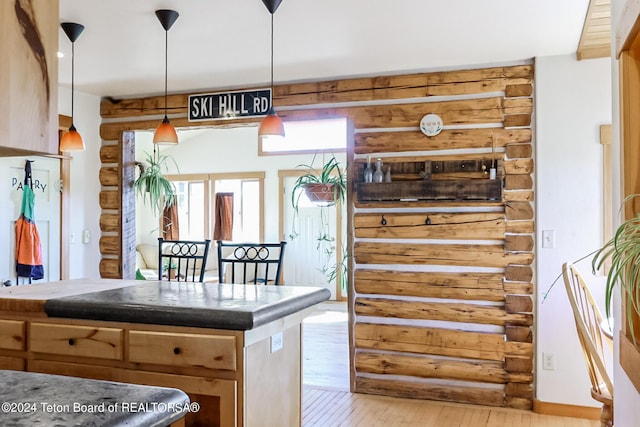 kitchen featuring light brown cabinets, light wood-type flooring, hanging light fixtures, and log walls