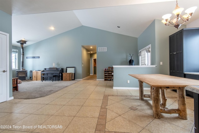 dining area with a wood stove, light tile patterned floors, vaulted ceiling, and a notable chandelier