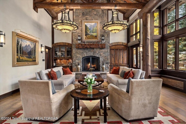 living room featuring a stone fireplace, hardwood / wood-style floors, beamed ceiling, and a towering ceiling