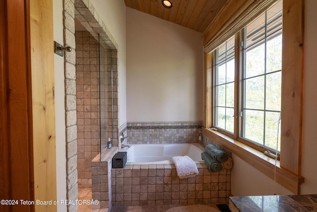 bathroom with a healthy amount of sunlight, tiled bath, and vaulted ceiling