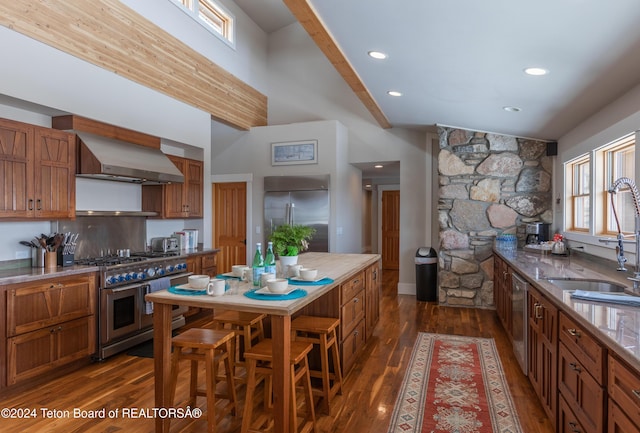 3470 W Mccollister Dr, Teton Village, WY 83025 - kitchen with high end appliances, wall chimney range hood, brown cabinets, dark wood finished floors, and a high ceiling
