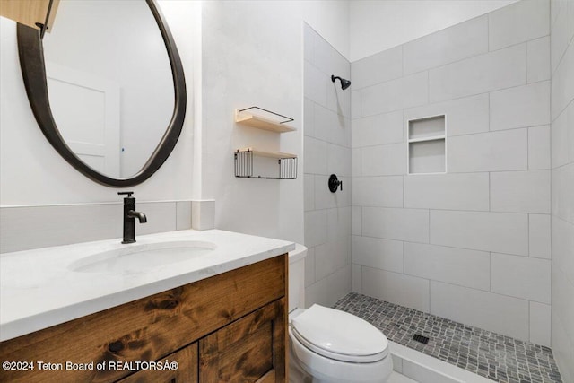 bathroom with toilet, tiled shower, and vanity