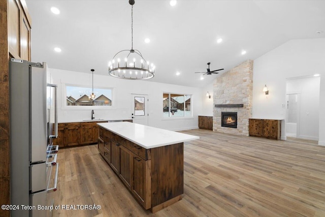 kitchen with stainless steel fridge, a fireplace, a kitchen island, pendant lighting, and light hardwood / wood-style flooring