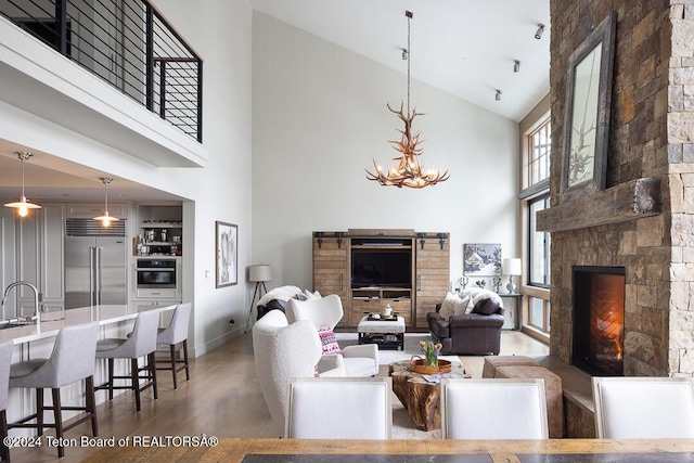 living room featuring sink, high vaulted ceiling, a chandelier, hardwood / wood-style floors, and a stone fireplace