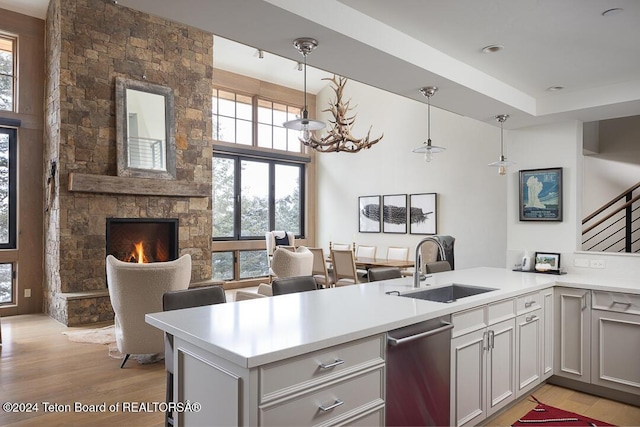 kitchen featuring sink, hanging light fixtures, stainless steel dishwasher, a fireplace, and kitchen peninsula