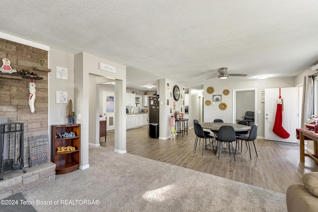 dining space featuring carpet flooring, ceiling fan, a stone fireplace, and a textured ceiling