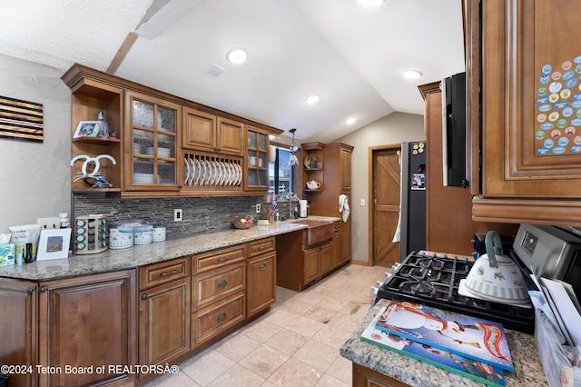 kitchen featuring lofted ceiling, sink, fridge, light tile patterned flooring, and light stone counters