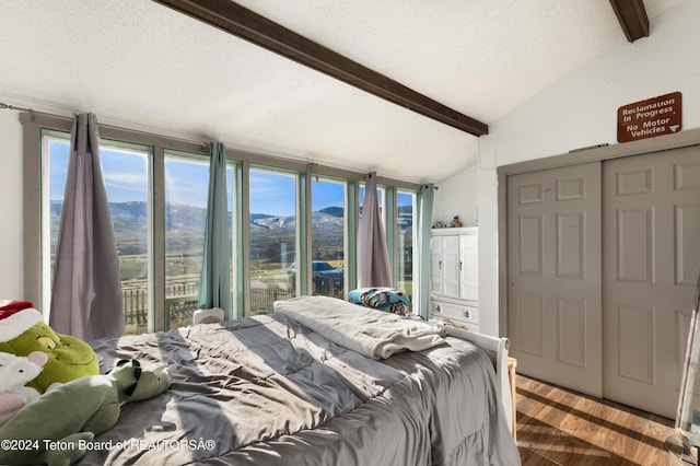 bedroom featuring a textured ceiling, hardwood / wood-style flooring, a mountain view, vaulted ceiling with beams, and a closet