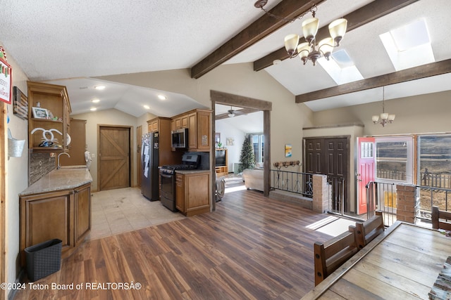 kitchen featuring vaulted ceiling with skylight, ceiling fan with notable chandelier, a textured ceiling, stainless steel appliances, and light hardwood / wood-style floors