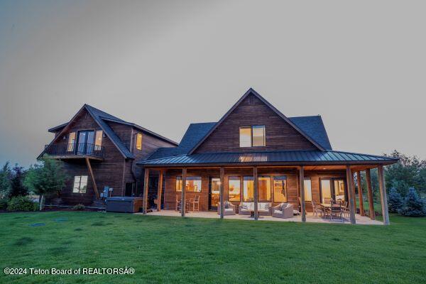 rear view of property with a balcony, a yard, a patio, and a hot tub