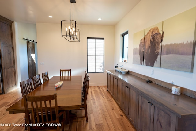 dining space with a notable chandelier, a barn door, and light wood-type flooring