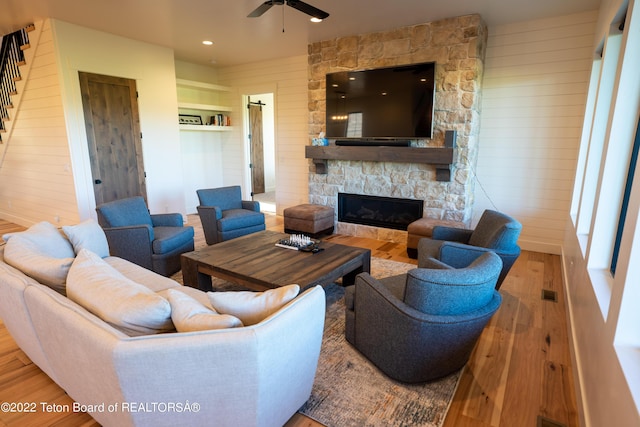 living room featuring a stone fireplace, ceiling fan, wooden walls, and hardwood / wood-style flooring