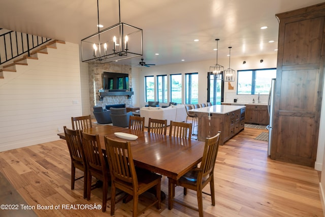 dining room featuring light hardwood / wood-style flooring, ceiling fan, and a stone fireplace