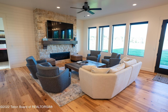 living room featuring a stone fireplace, ceiling fan, and light hardwood / wood-style floors