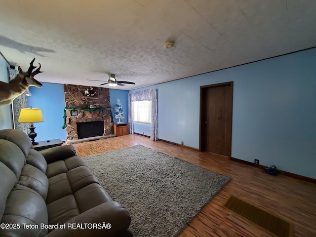 living room featuring a stone fireplace, ceiling fan, and hardwood / wood-style floors