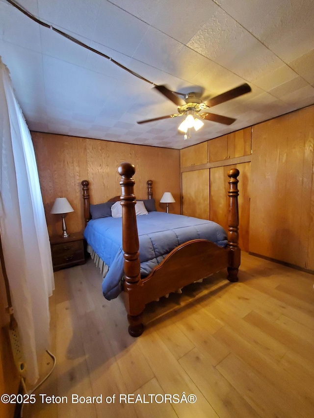 bedroom featuring ceiling fan, wood walls, and light wood-type flooring