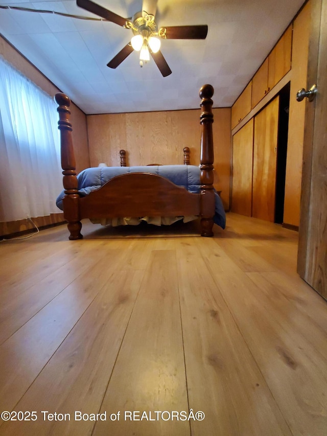 unfurnished bedroom featuring ceiling fan, a closet, wooden walls, and light hardwood / wood-style flooring